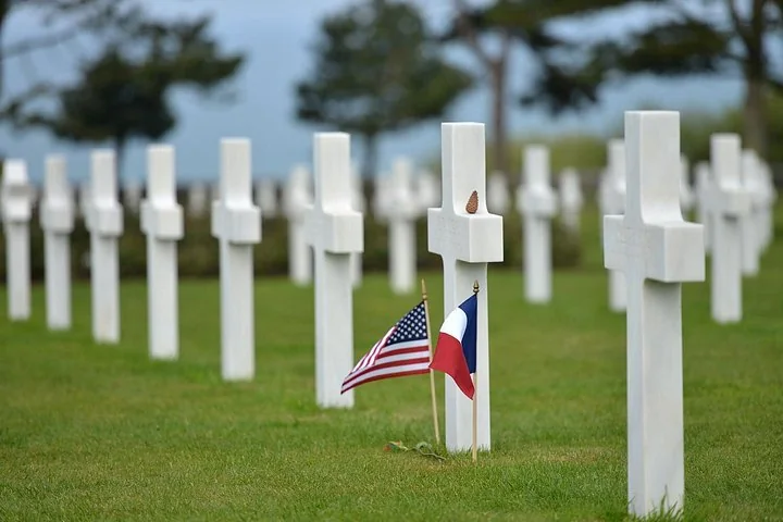 White crosses on a lawn, with small American and French flags planted at the foot of one