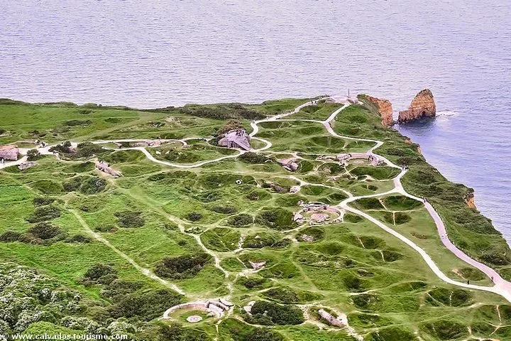 Aerial view of a green headland pitted with craters and crossed by footpaths above the sea