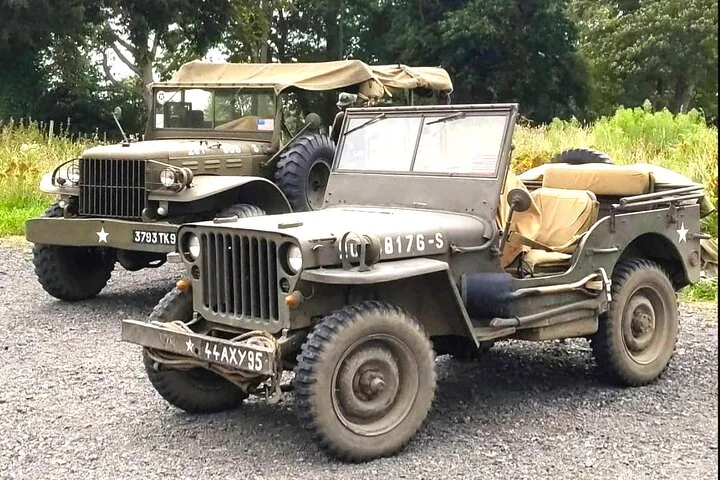 Two restored WWII US Army vehicles, a jeep and a covered Dodge truck, parked on gravel
