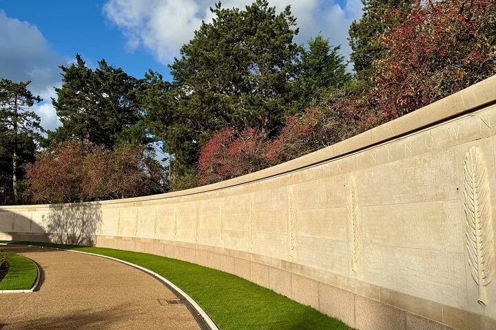 A long curved stone wall inscribed with names beside a garden path and trees