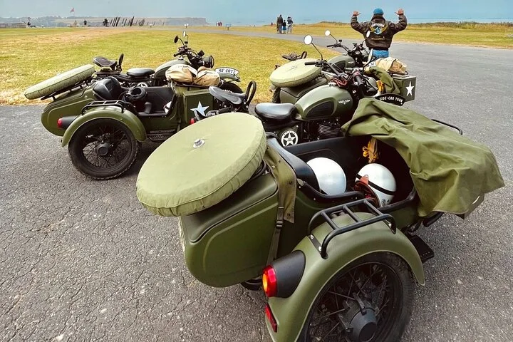 Olive-green vintage motorcycles with sidecars parked on a coastal road
