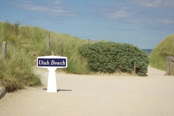 A white Utah Beach sign on a sandy path between grassy dunes