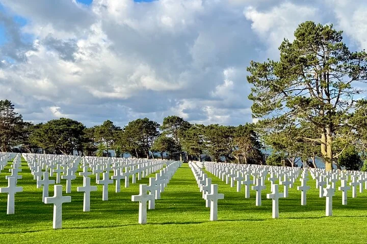 Long rows of white marble crosses on a lawn under tall pines