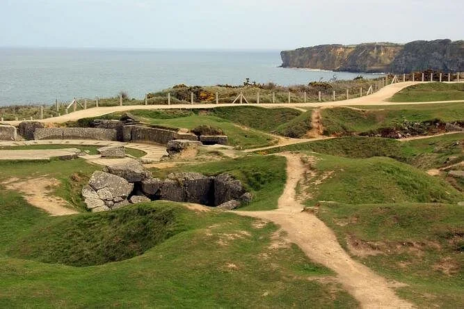 Grassy bomb craters and broken concrete on a clifftop, with cliffs and sea behind