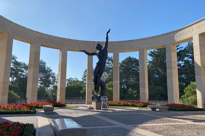 A bronze statue of a young man with arms raised, in front of a curved stone colonnade